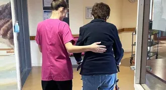 Une professionnelle accompagne une personne âgée dans un couloir