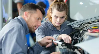 Une apprentie regarde le moteur d'une voiture avec son maître d'apprentissage