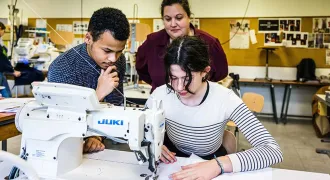 Deux élèves travaillent sur un vêtement avec l'aide de leur enseignante