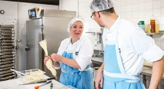 Deux agents de restaurations préparent des plats dans une cuisine de lycée