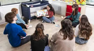 Un groupe de stagiaires adultes autour d'une stagiaire présentant un livre pour enfants