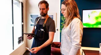 Un homme avec un tablier explique le fonctionnement d'une tablette à une femme