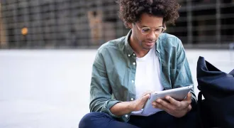 Un étudiant assis dehors regarde une tablette