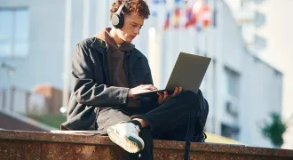Un étudiant regarde son portable dehors, devant des drapeaux de différents pays