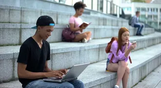 Des élèves sont assis sur des marches à lire ou à écrire sur un portable
