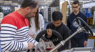 Un enseignant parle avec un groupe d'élèves autour d'un prototype de voiture