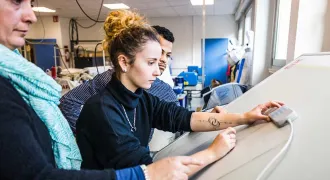Deux élèves travaillent sur une table à dessin accompagnés de leure professeure