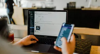 Une personne regarde son écran d'ordinateur et tient un portable dans une main
