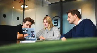 Une étudiante et un étudiant regardent un portable avec leur maître de stage à côté