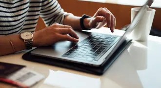 Des mains tapent sur un ordinateur à une table à côté d'une tasse