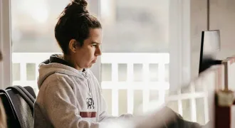 Une lycéenne de profil regarde son ordinateur chez elle