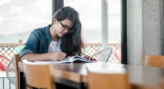 Une lycéenne écrit sur un cahier à une table