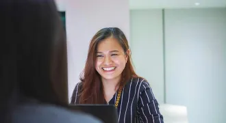 Une femme derrière un ordinateur sourit à une femme en face d'elle à la même table