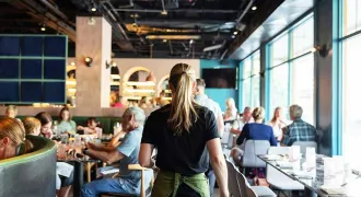Une serveuse de dos marche dans une salle de restaurant remplie de client