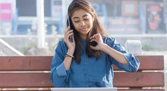 Une étudiante sur un bac téléphone et regarde son ordinateur en même temps