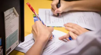 Des mains de deux personnes écrivent sur des feuilles sur une table