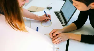 Deux femmes travaillent sur une table et annotent une feuille avec un dessin géométrique