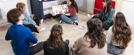 Un groupe de stagiaires adultes autour d'une stagiaire présentant un livre pour enfants