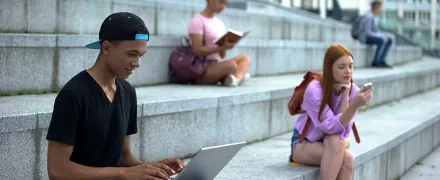 Des élèves sont assis sur des marches à lire ou à écrire sur un portable