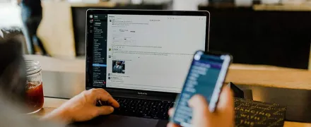 Une personne regarde son écran d'ordinateur et tient un portable dans une main