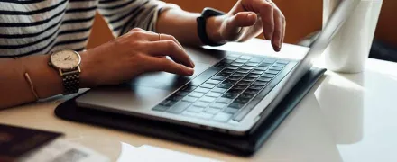 Des mains tapent sur un ordinateur à une table à côté d'une tasse