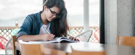 Une lycéenne écrit sur un cahier à une table