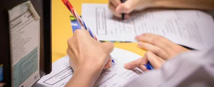 Des mains de deux personnes écrivent sur des feuilles sur une table