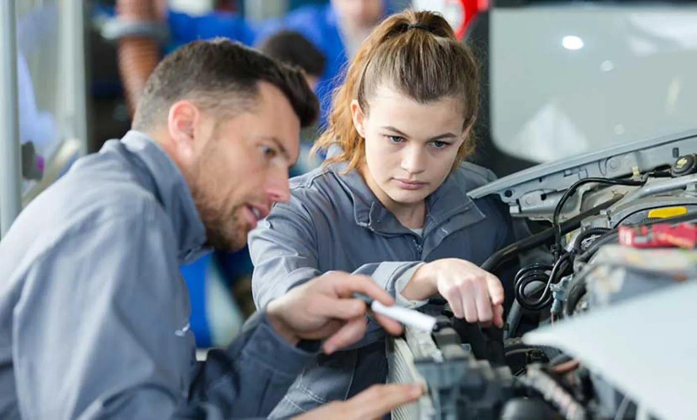 Une apprentie regarde le moteur d'une voiture avec son maître d'apprentissage