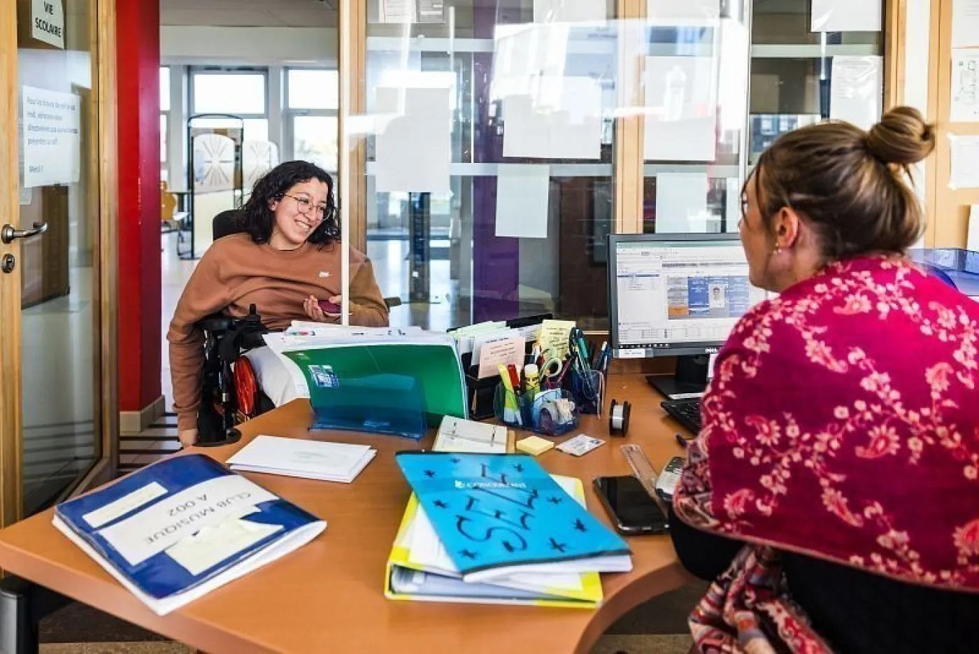 Une lycéenne en fauteuil roulant électrique lors d'un échange avec une conseillère principale d'éducation dans le bureau de la vie scolaire.
