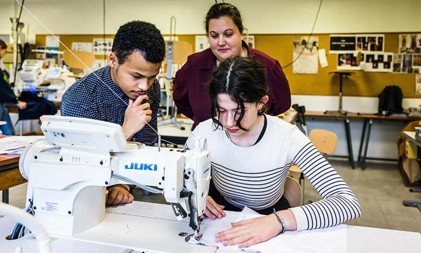 Deux élèves travaillent sur un vêtement avec l'aide de leur enseignante