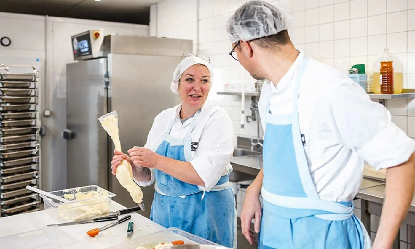 Deux agents de restaurations préparent des plats dans une cuisine de lycée