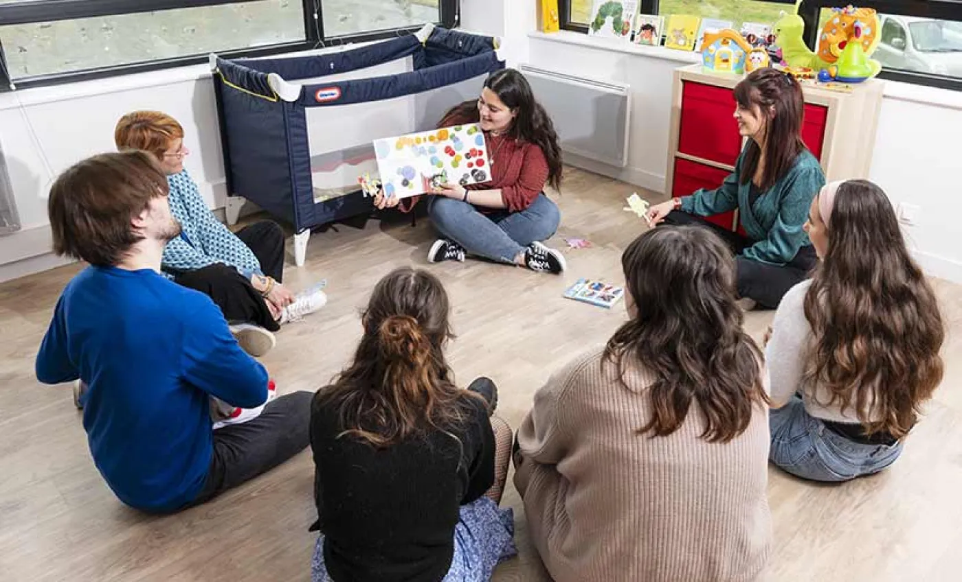 Un groupe de stagiaires adultes autour d'une stagiaire présentant un livre pour enfants