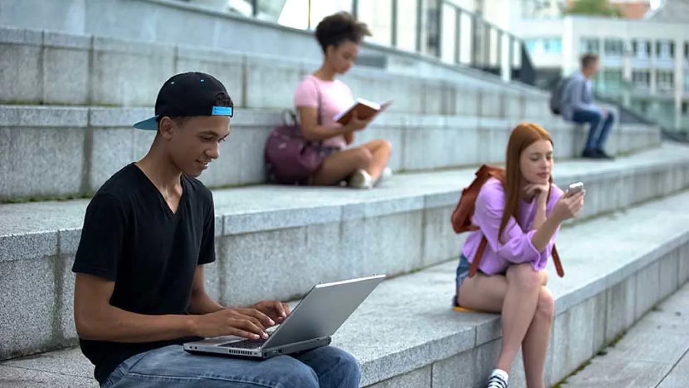 Des élèves sont assis sur des marches à lire ou à écrire sur un portable
