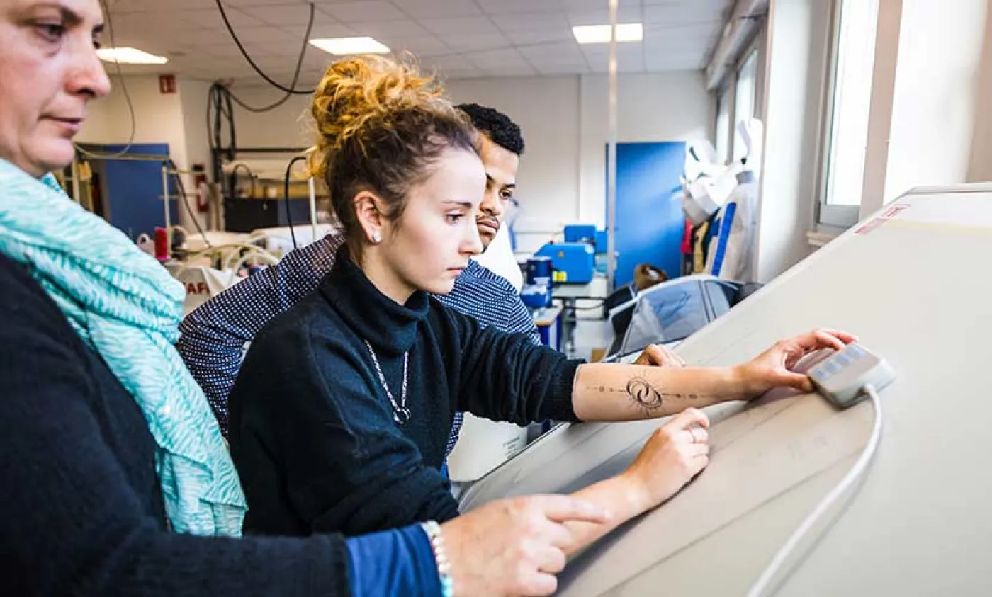 Deux élèves travaillent sur une table à dessin accompagnés de leure professeure