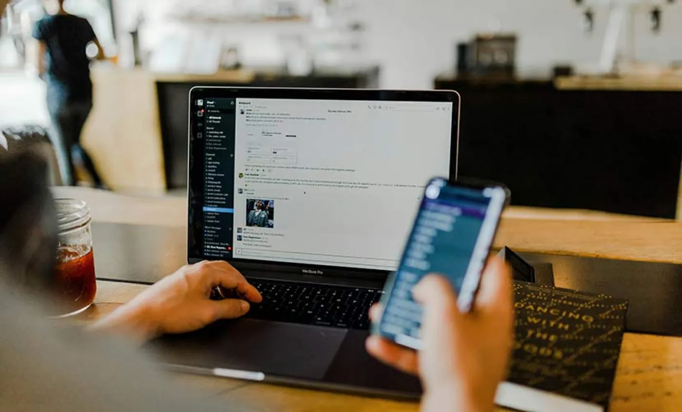 Une personne regarde son écran d'ordinateur et tient un portable dans une main