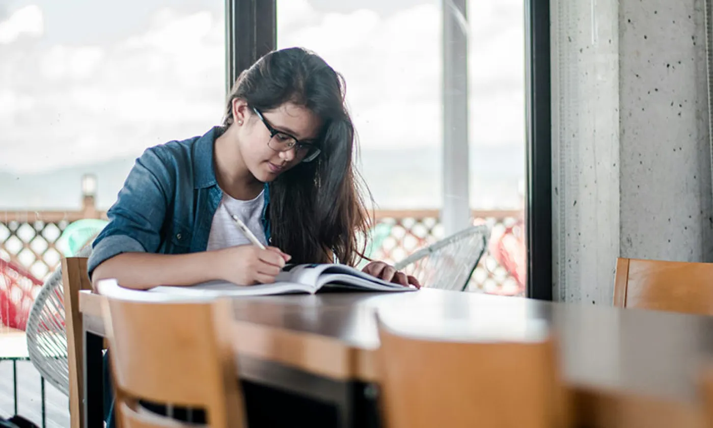 Une lycéenne écrit sur un cahier à une table