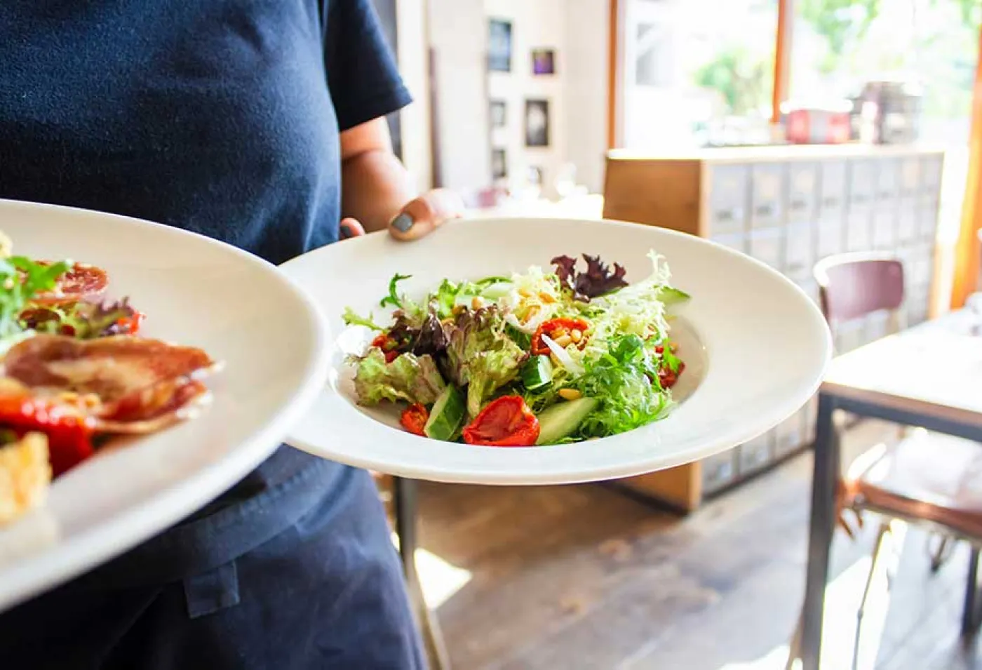 Des mains d'une serveuse apportent deux plats dans un restaurant