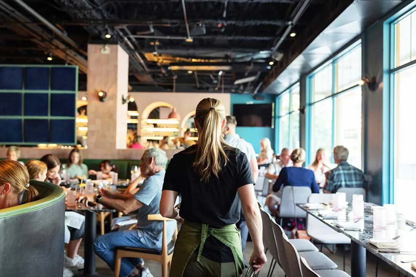 Une serveuse de dos marche dans une salle de restaurant remplie de client
