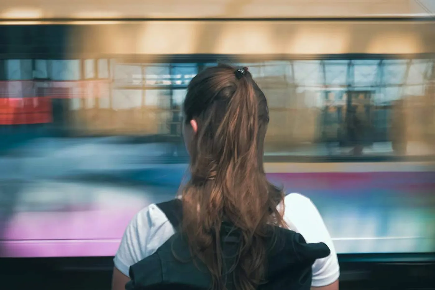 Une jeune fille avec un sac à dos devant un train