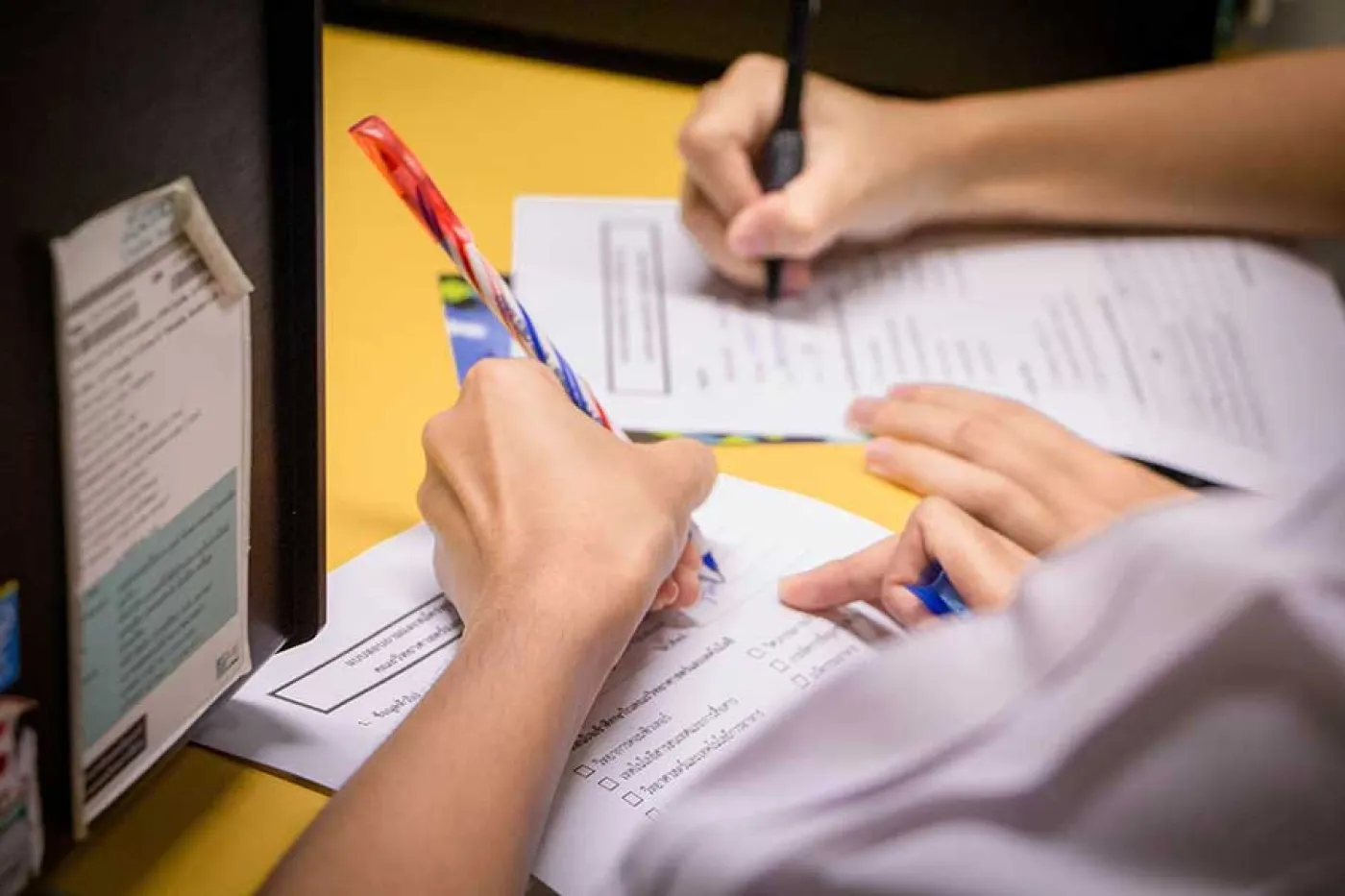 Des mains de deux personnes écrivent sur des feuilles sur une table