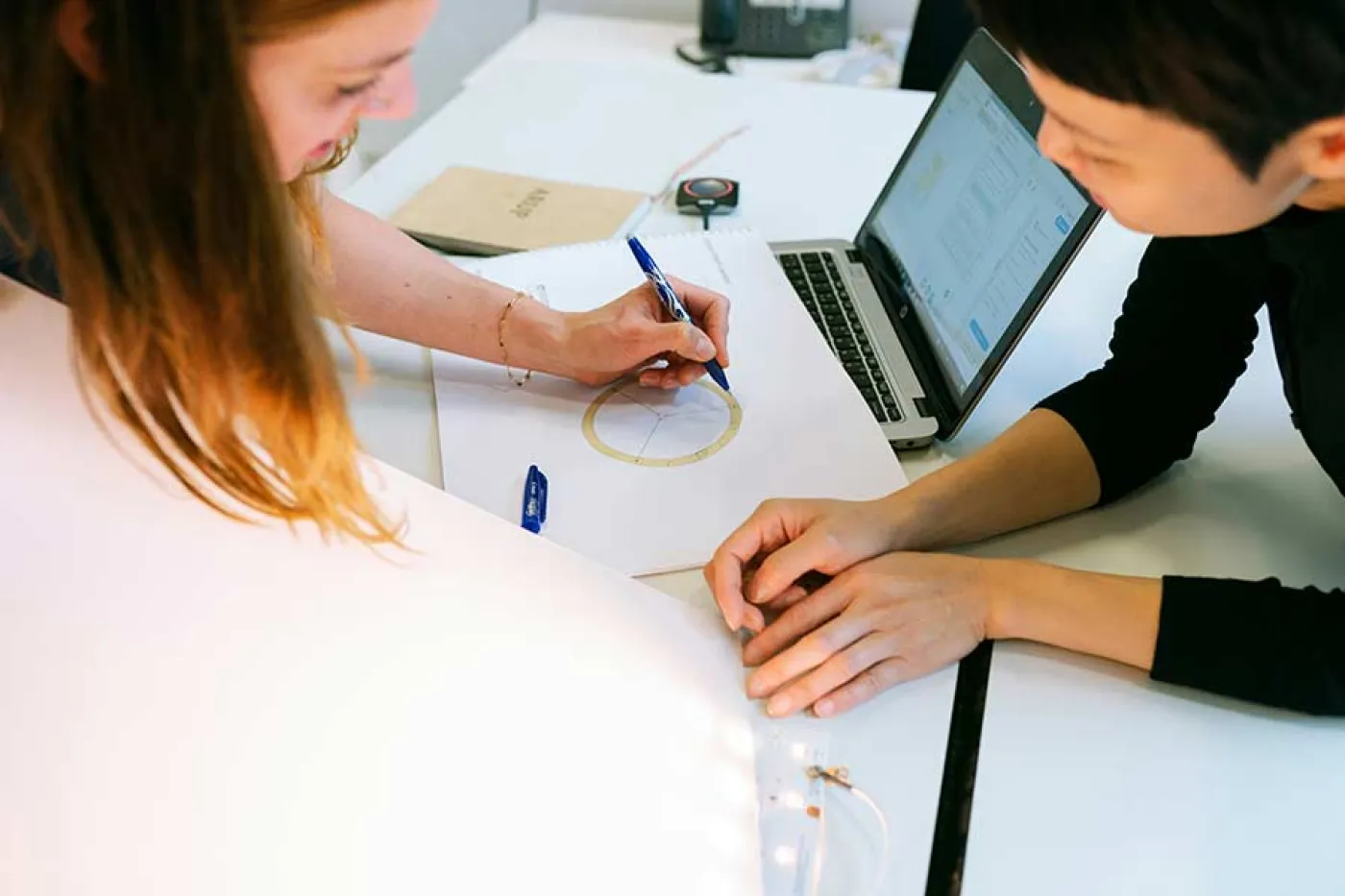 Deux femmes travaillent sur une table et annotent une feuille avec un dessin géométrique