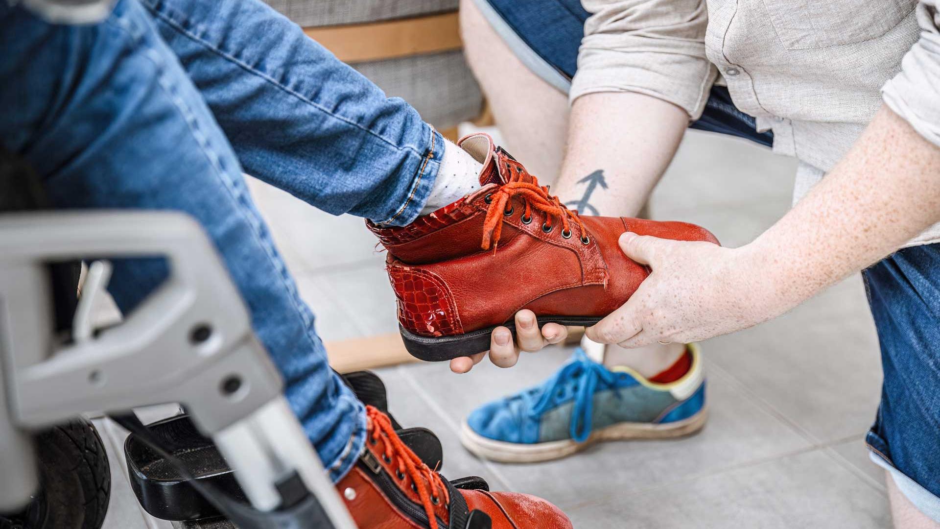 Un accompagnant éducatif et social aide une personne handicapée à mettre sa chaussure