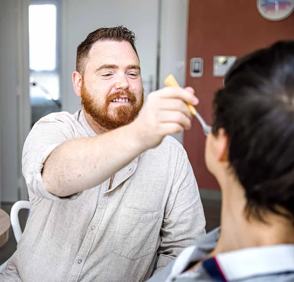 Un professionnel aide une jeune homme handicapé à prendre son repas