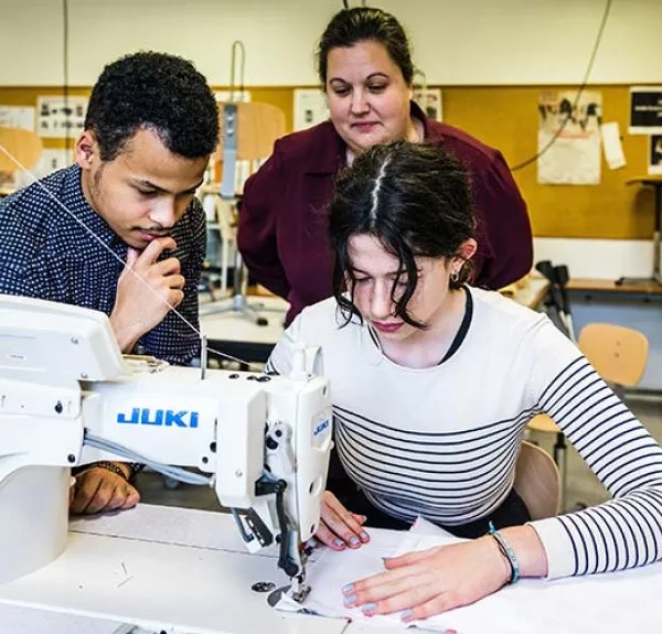 Deux élèves travaillent sur un vêtement avec l'aide de leur enseignante