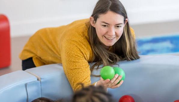 une éducatrice de jeunes enfants joue à un jeu de balles avec des enfants.