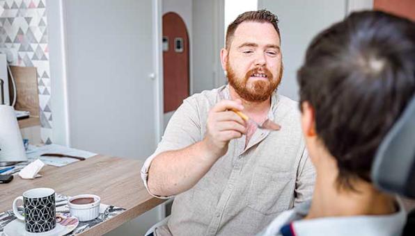 Un accompagnant éducatif et social donne à manger à une personne en fauteuil tient la main d'une personne âgée
