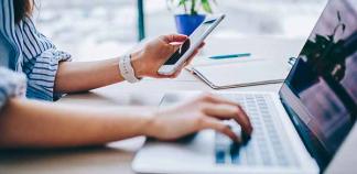 Des mains écrivent sur un ordinateur et tiennent un smartphone