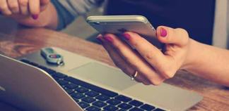 Des mains tiennent un smartphone devant un ordinateur portable