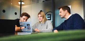 Une étudiante et un étudiant regardent un portable avec leur maître de stage à côté