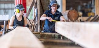Une opératrice de scierie déplace des planches de bois à l'aide d'un bras mécanique